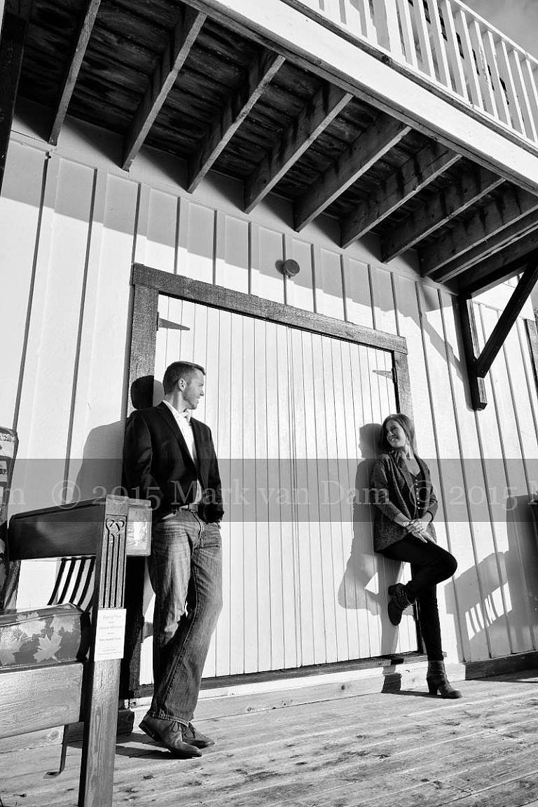 Stylish couple leans against boathouse door at Leacock Museum engagement photography session