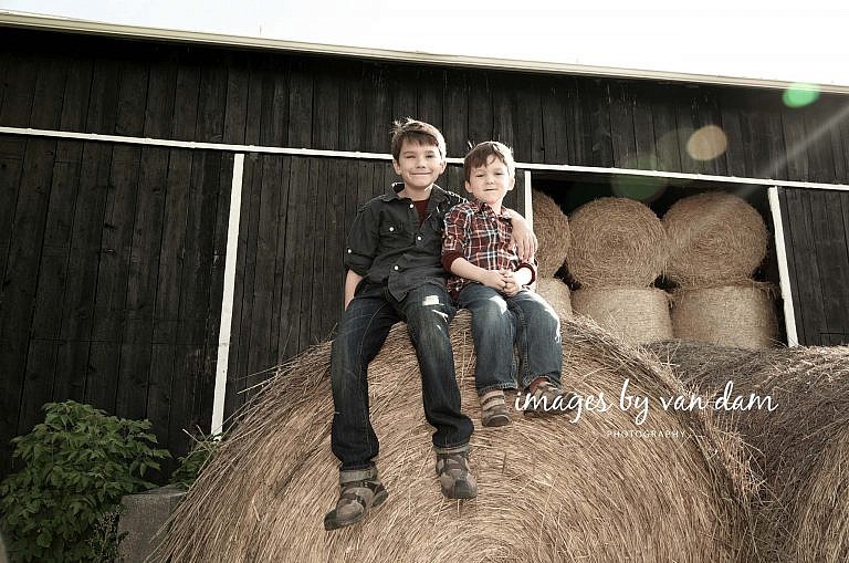 Two young brothers perch on top of a giant hay bale stayner photographer barrie photographer family portraits wasaga photographer collingwood photographer