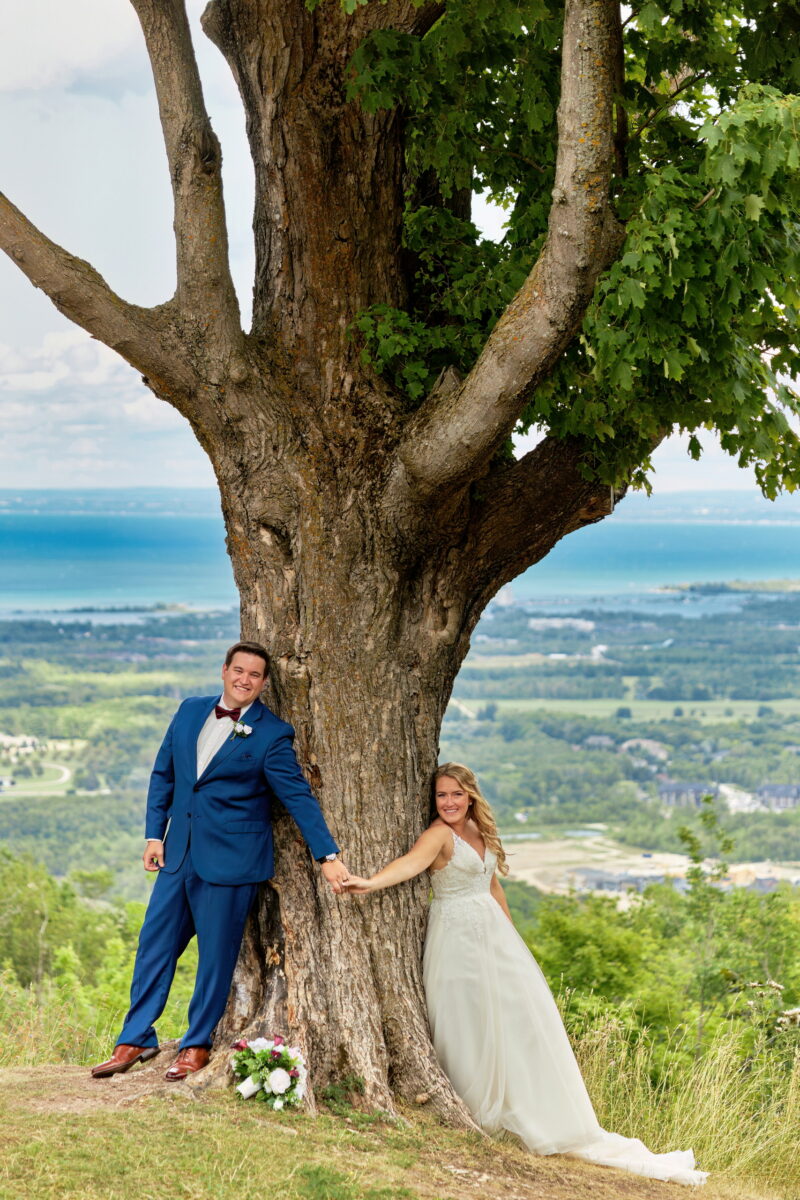 Bride and groom Hold Hands Across a Magnificent Hardwood Tree at the Top of Blue Mountain