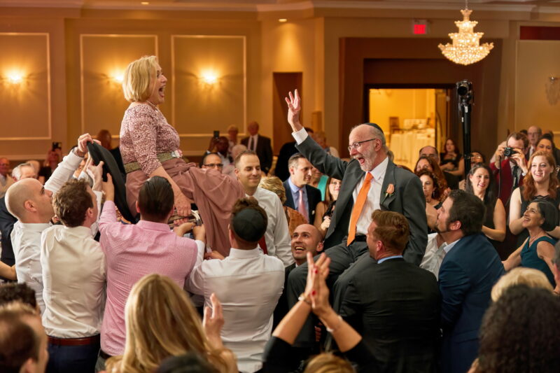 To their delight, parents of the newlyweds are hoisted up on chairs above the dance floor for the Jewish Hora dance at a Toronto wedding