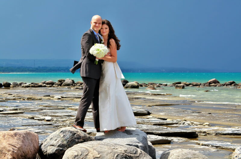 Bride in Groom on Rocks at Craigleith Beach with Georgian Bay and Stormy sky in background