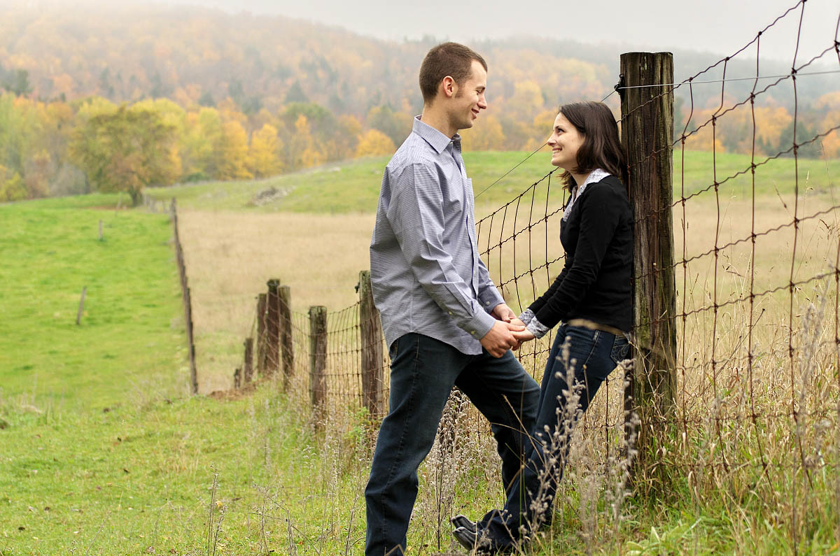 Young couple in farm field by fence at country themed engagement session