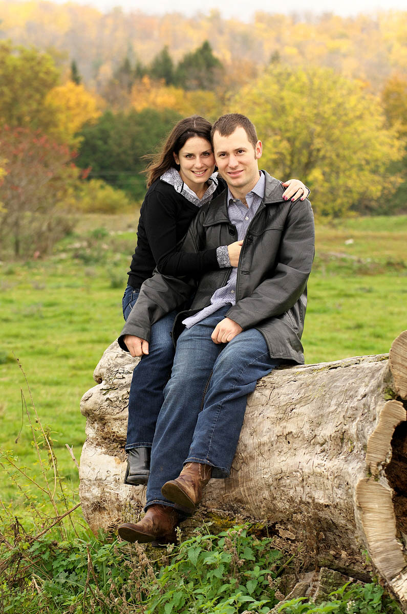 Young couple snuggles on boulder at country themed engagement session on farm