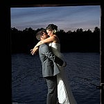 At dusk, groom lifts his bride in his arms outside boathose on Stoney Lake