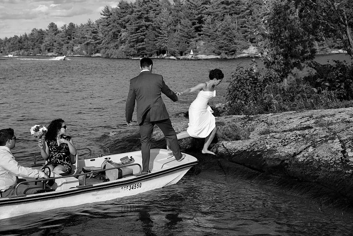 bride climbs onto island from boat for stoney lake wedding photography session