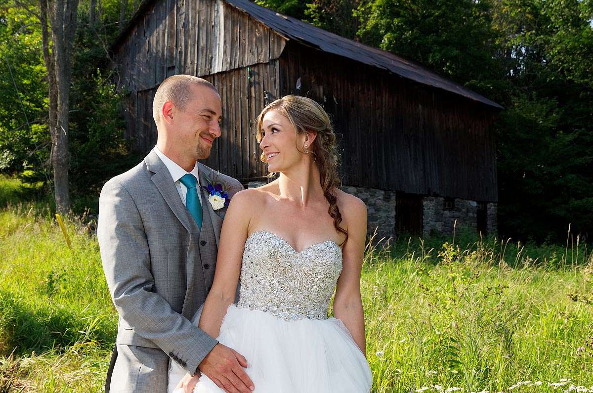 Bride and Groom Embrace in Meadow by Rustic Barn in Haliburton, Ontario