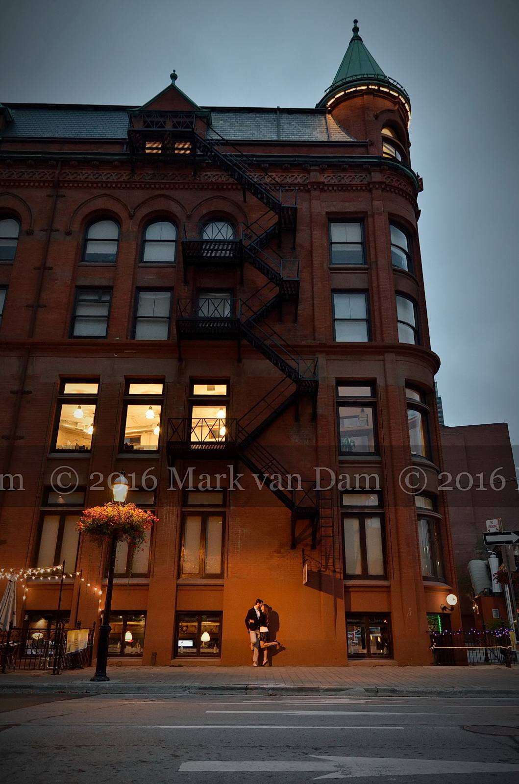Engaged couple kisses in front of Gooderham Flatiron Building