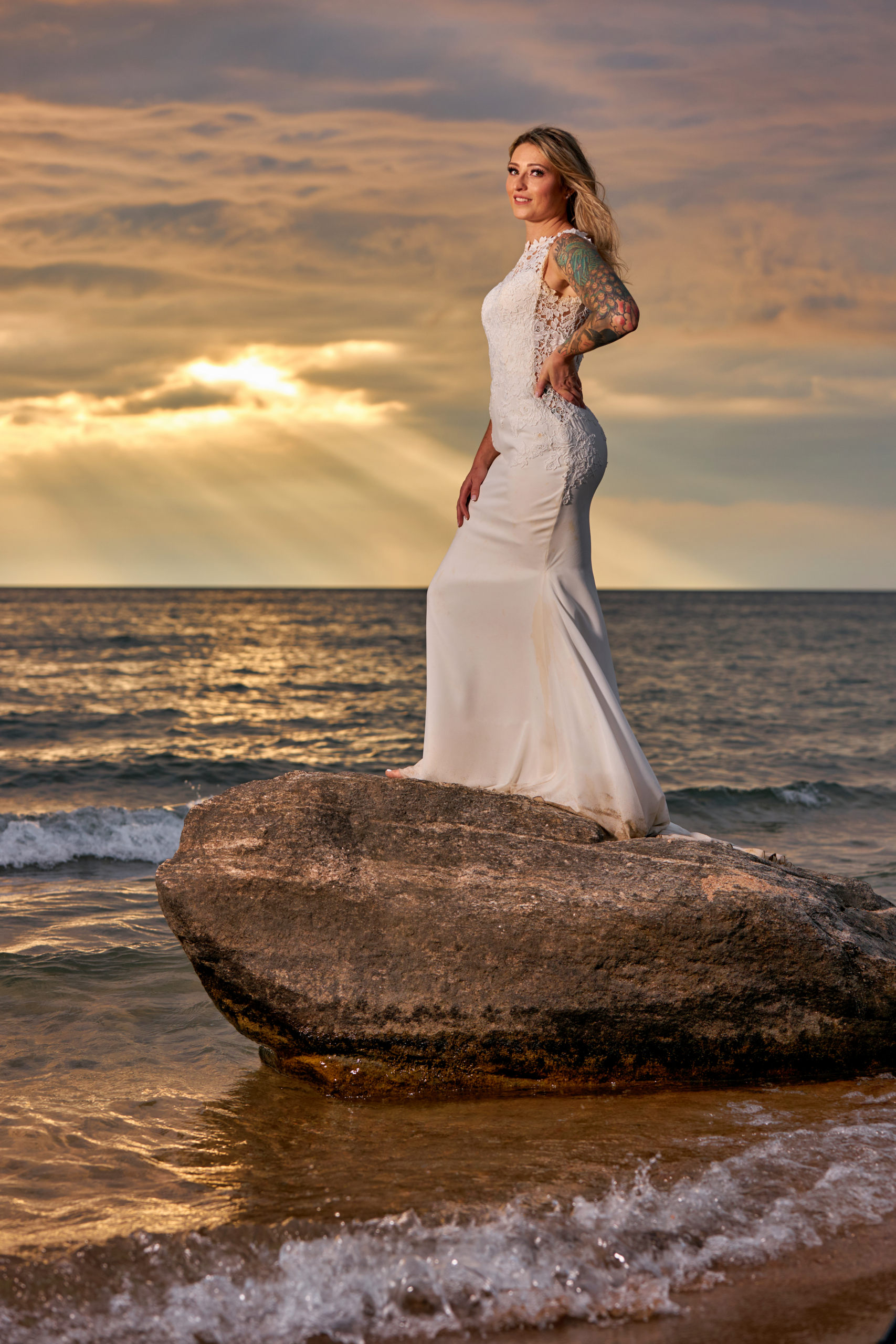 Bride Standing on Large Rock in water with magnificent sunset behind her