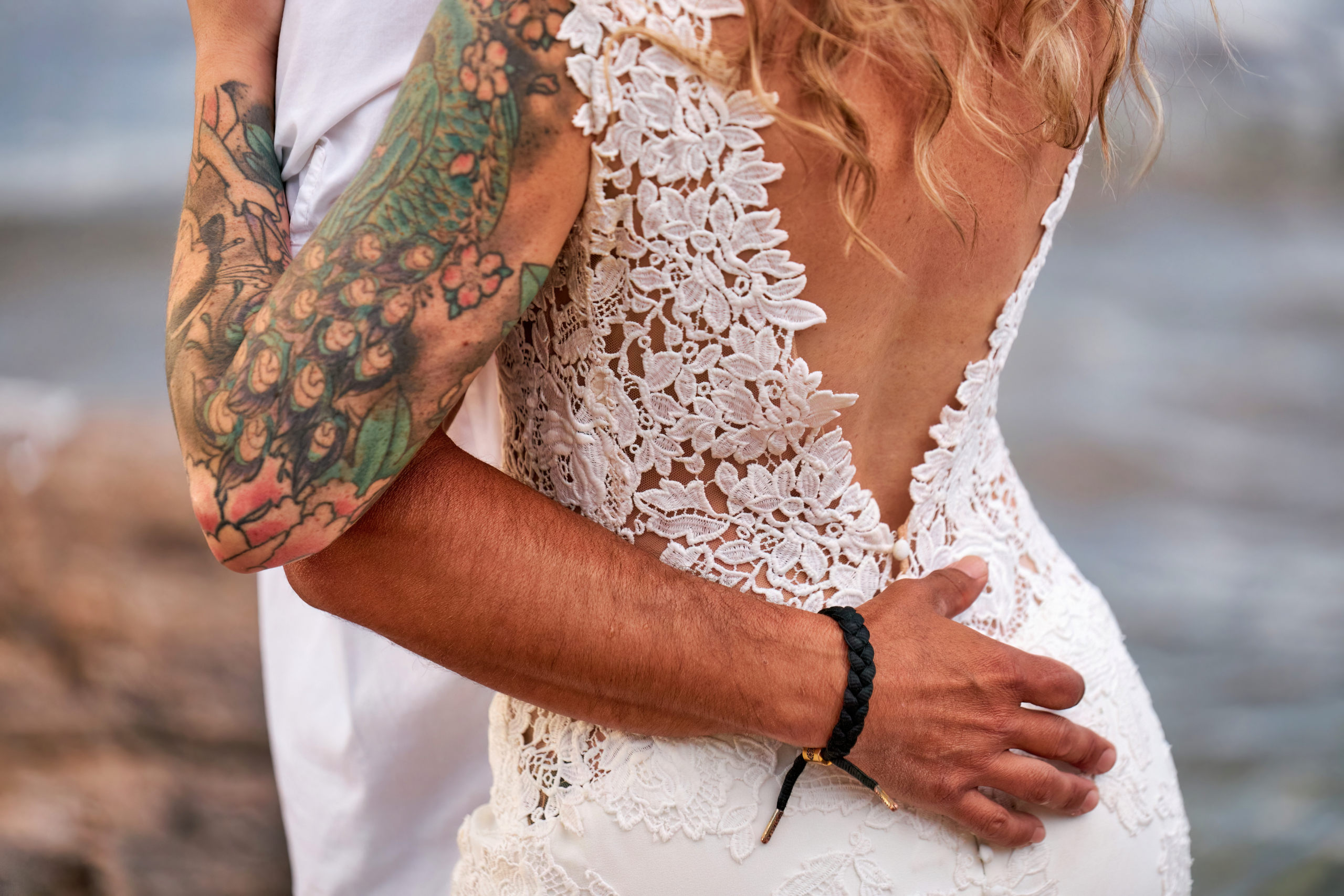 Close up of a Groom's Arm wrapped tightly around the small of his wife's back at the beach