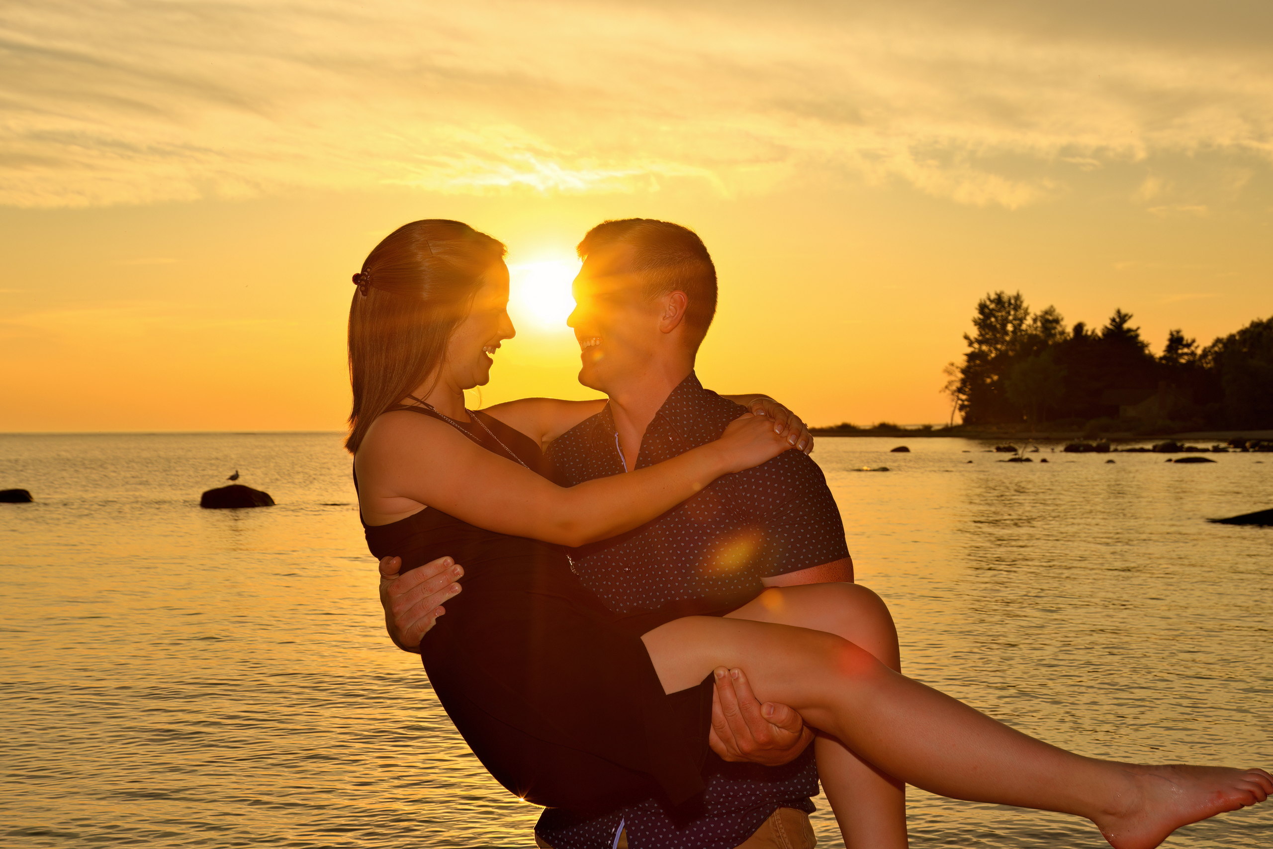 A young man lifts his A young woman jumps into her fiancé's arms right after he asks her to marry him in front of Blue Mountain in Collingwood into his arms at sunset in front of Georgian Bay